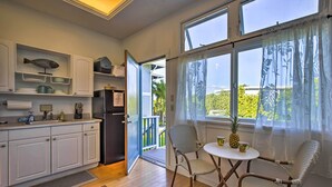 A compact kitchen with white cabinets, a refrigerator, and a dining area with wicker chairs and a small table. - 1 Mile to Magic Sands Beach: Kailua-kona Cottage (Kailua-Kona)
