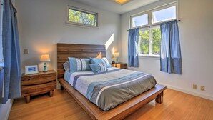 A bedroom with a wooden bed, two bedside tables with lamps, a window with curtains, and a view of greenery outside. - 1 Mile to Magic Sands Beach: Kailua-kona Cottage (Kailua-Kona)