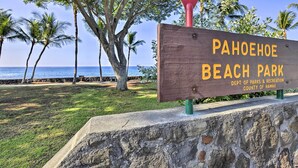 A wooden sign for Pahohoe Beach Park with a view of the ocean and palm trees in the background. - 1 Mile to Magic Sands Beach: Kailua-kona Cottage (Kailua-Kona)