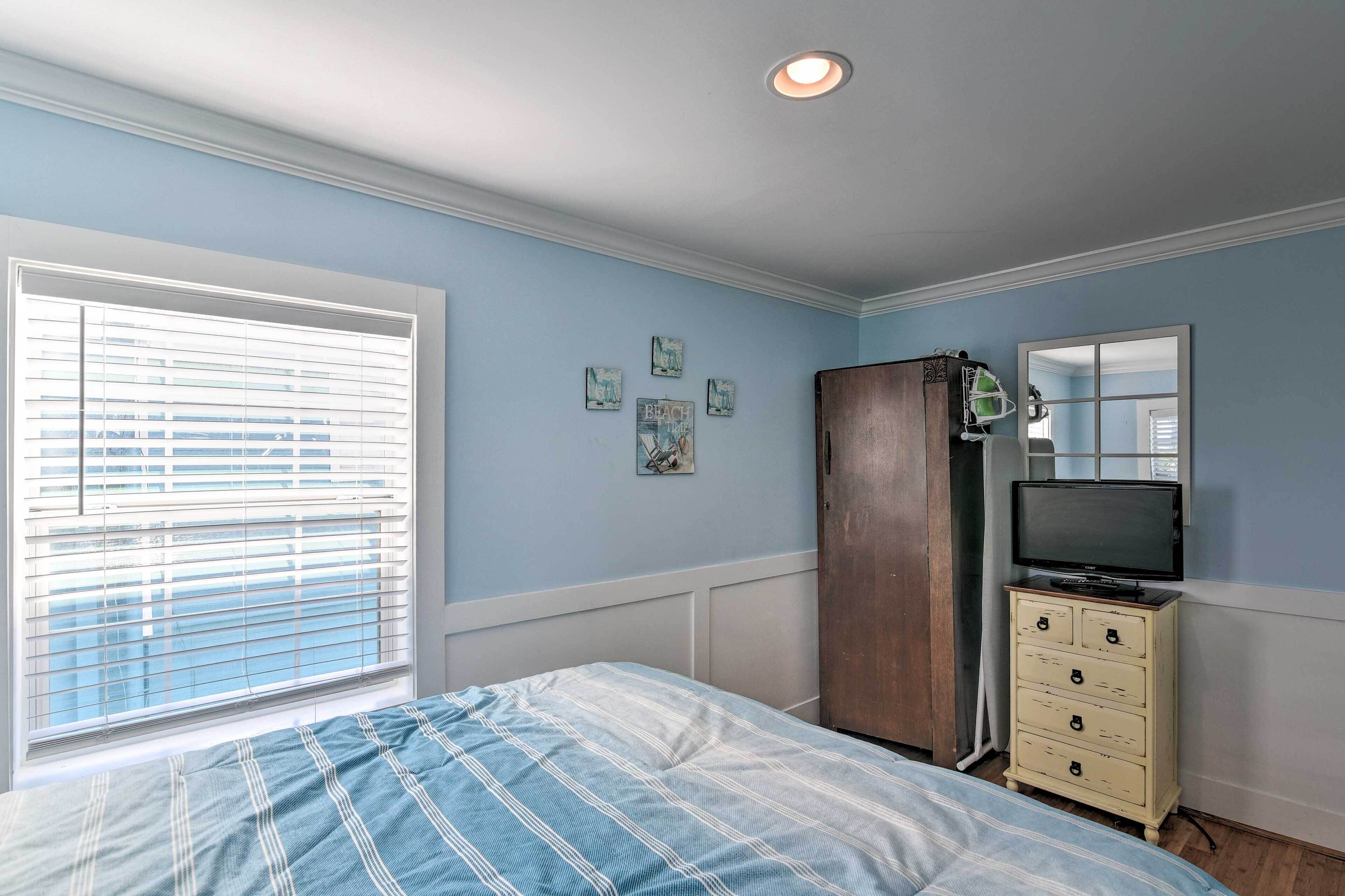 A bedroom with a bed, dresser, television, and wall art.