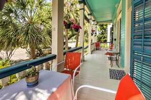 A covered outdoor seating area with a table and chairs, surrounded by palm trees and hanging flower baskets. - Vintage Galveston Apt < 1/2 Mi to Porretto Beach! (Galveston)