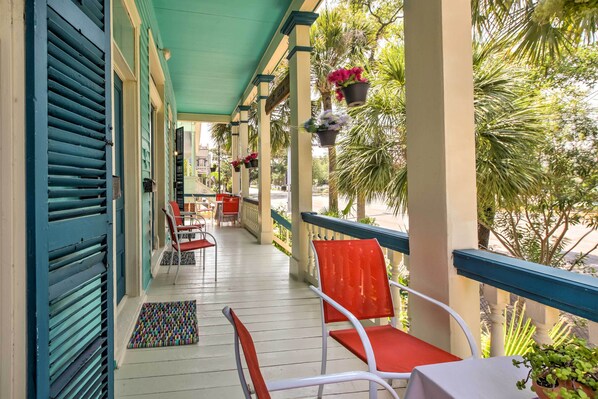 A covered porch with red chairs and a table, potted plants, and a view of palm trees. - Vintage Galveston Apt < 1/2 Mi to Porretto Beach! (Galveston)