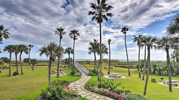 A landscaped garden with palm trees, a stone pathway, and outdoor seating areas. - Heated Pool + Gulf View: Galvestonian Resort Condo (Galveston)