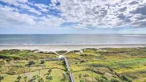 A coastal landscape with a beach, grassy areas, and a wooden boardwalk. - Heated Pool + Gulf View: Galvestonian Resort Condo (Galveston)