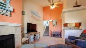 A living room with a fireplace, television, and a dining area with a staircase leading to another level. - Balcony & Pool Access: Condo in Galveston! (Galveston)