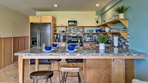 Une cuisine moderne dotée de plans de travail en granit, d’appareils électroménagers en acier inoxydable, d’armoires en bois et d’un îlot central avec des tabourets de bar.