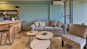 Un espace de vie moderne comprenant un coin cuisine, un canapé, une table basse et un fauteuil à motifs.