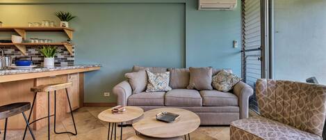 Un espacio habitable moderno con zona de cocina, sofá, mesa de centro y sillón estampado.