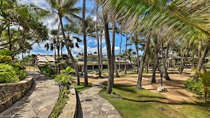 Un complexe hôtelier tropical doté d’un sentier dallé, de palmiers et d’un bâtiment dont le toit est incurvé.