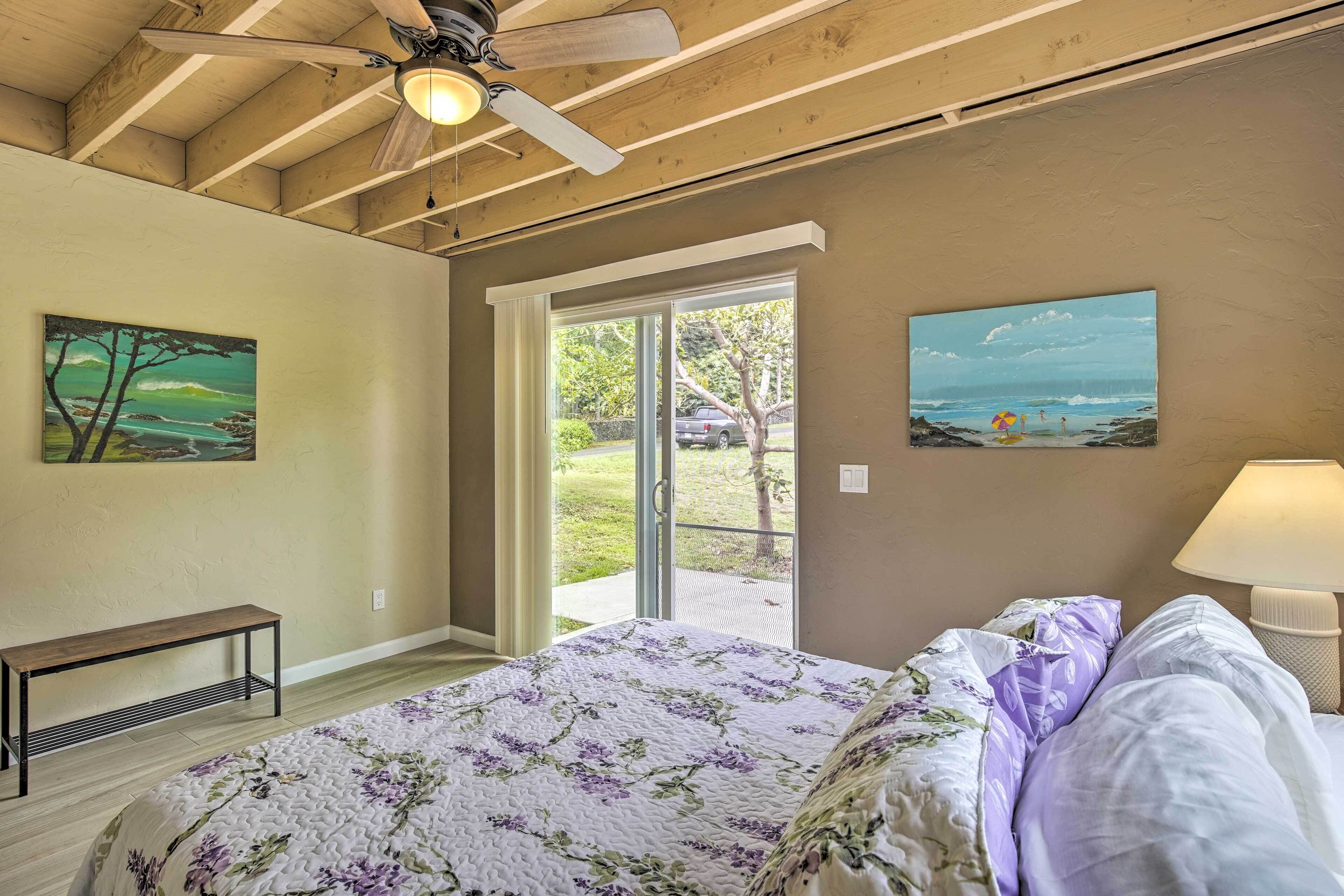 A bedroom with a bed, a bench, a ceiling fan, and two paintings on the walls.