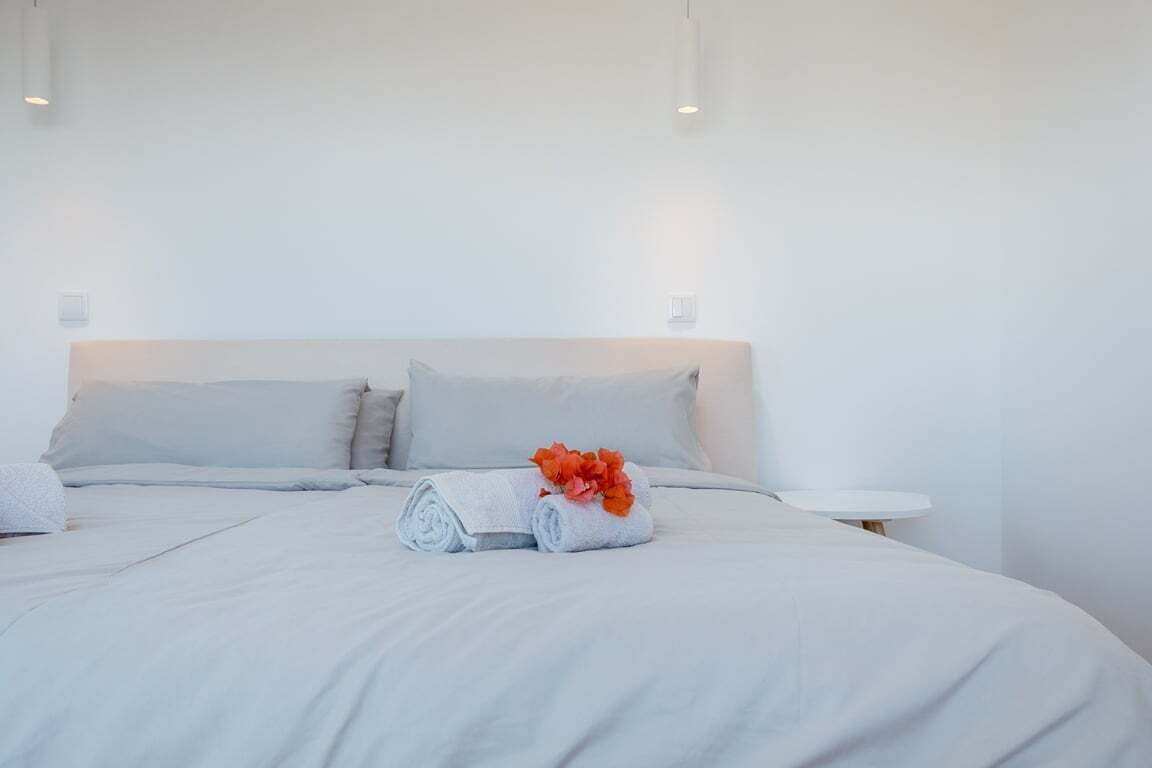 Una cama bien hecha con sábanas blancas y una toalla enrollada con flores naranjas.