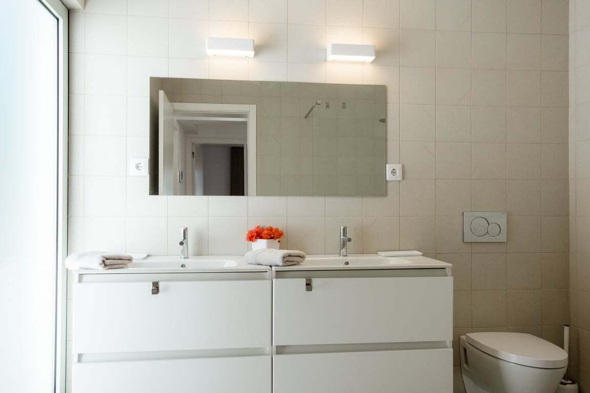A modern bathroom with a double sink vanity, a toilet, and a mirror above the vanity.