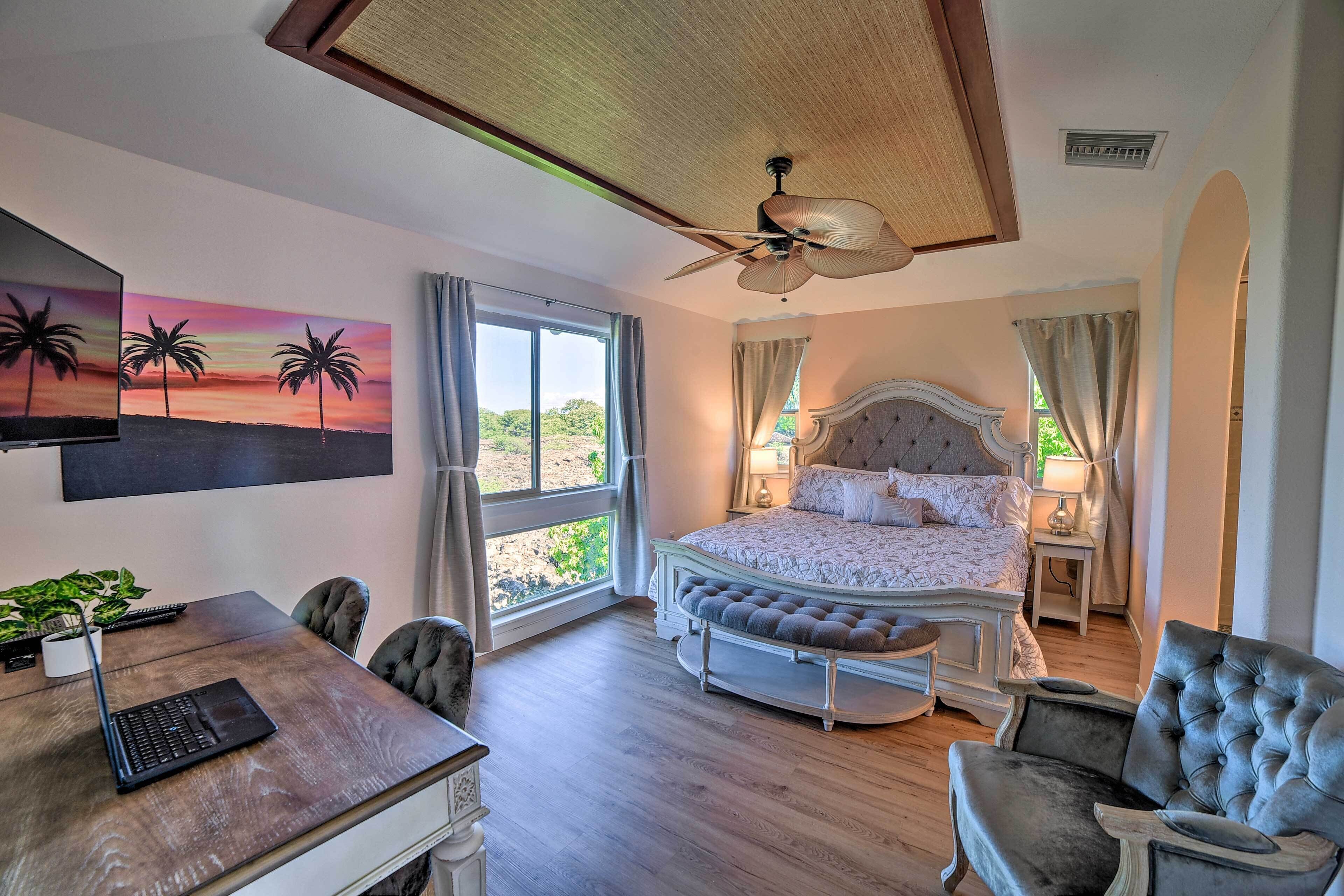A bedroom with a large bed, a desk with a laptop, a chair, and a ceiling fan.