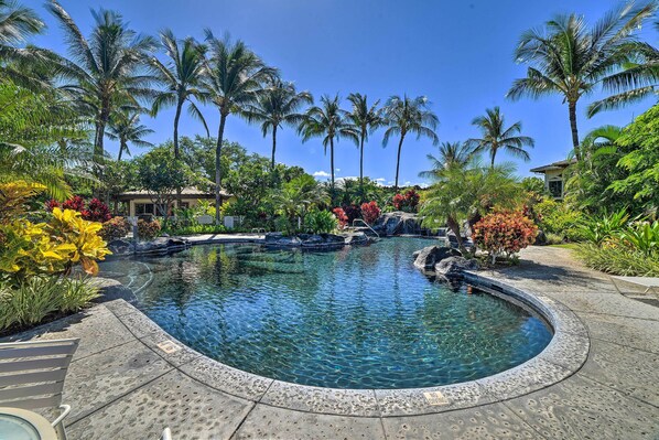 Une piscine circulaire à l’eau claire, entourée de plantes tropicales et de palmiers.