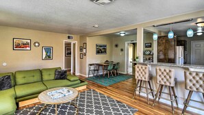 A living room with a green sofa, a coffee table, and a patterned rug. There is a dining area with a table and chairs, and a kitchen area with bar stools and a refrigerator. - Vintage Downtown Vegas Retreat < 3 Mi to Strip! (Las Vegas)