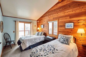 Une pièce chaleureuse avec deux lits, des murs en bois et de grandes fenêtres.