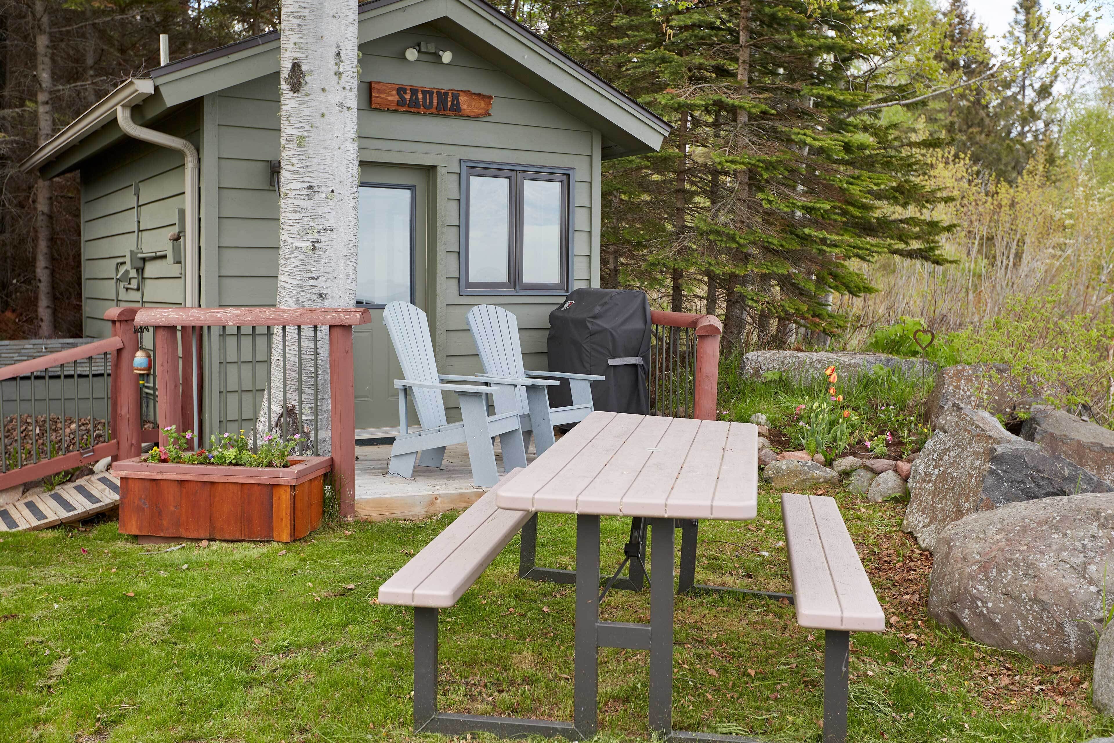 Eine Hütte mit einer Terrasse, zwei Adirondack-Stühlen, einem Picknicktisch und einem Schild für die Sauna.