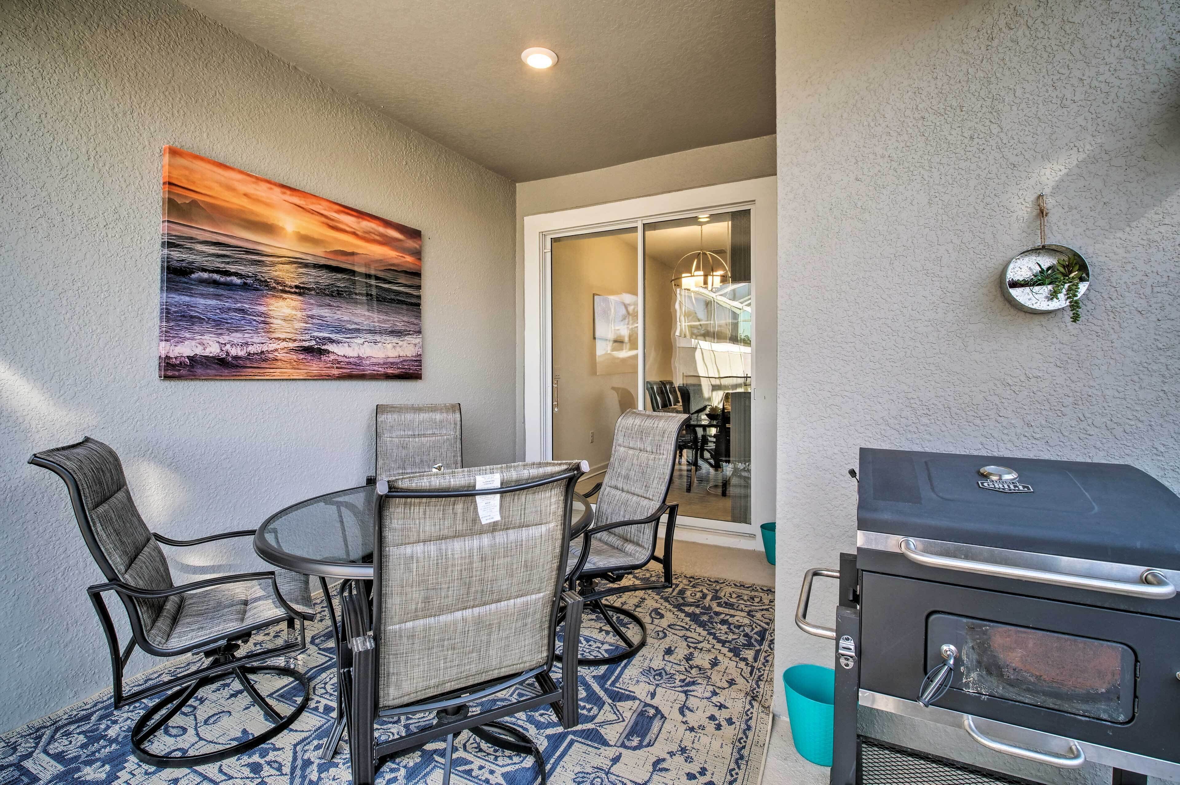 A patio with a glass table and chairs, a barbecue grill, and a painting on the wall.