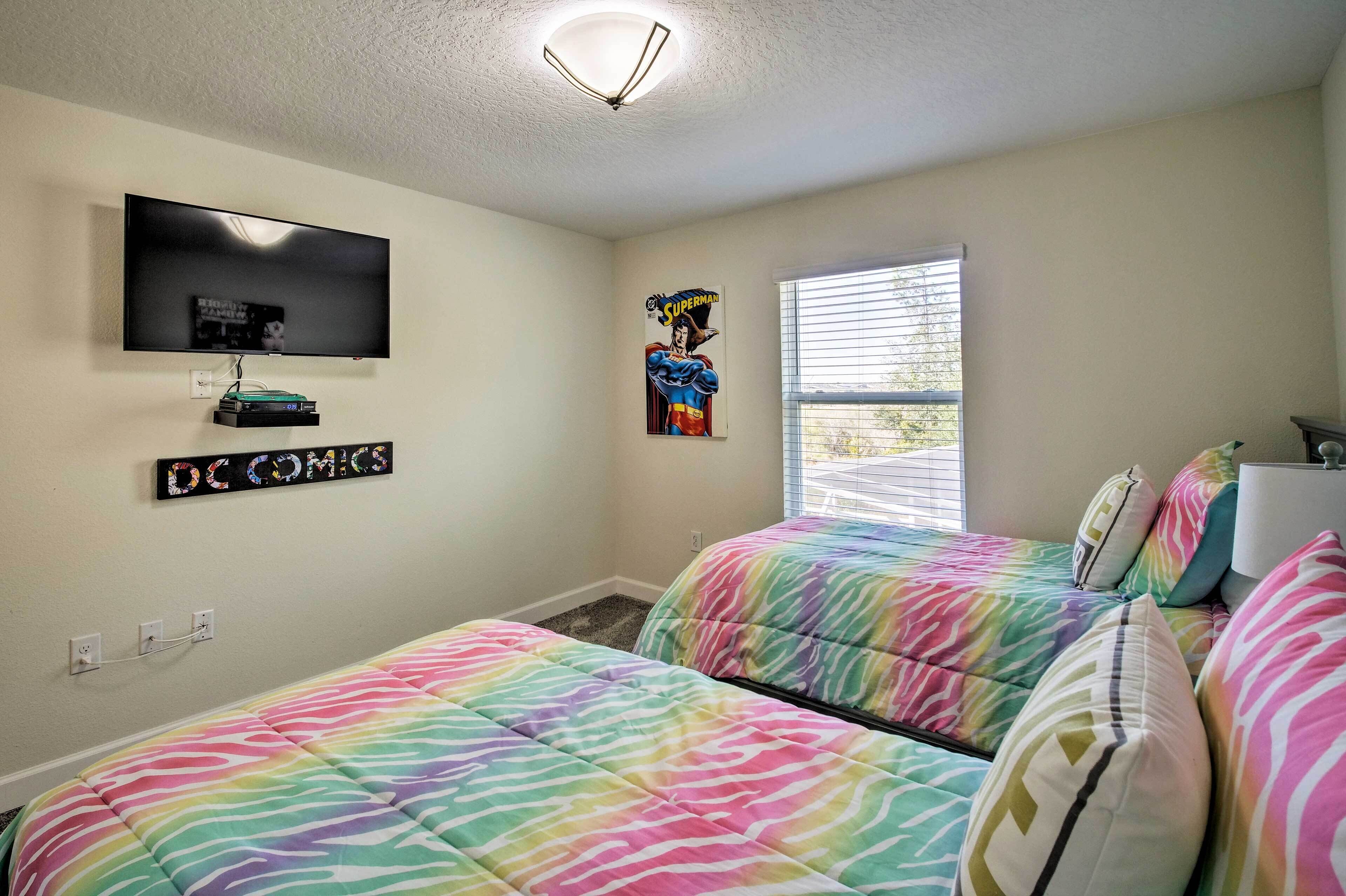 A bedroom with two beds, a TV mounted on the wall, and a window with blinds.