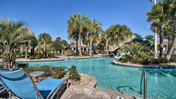 A swimming pool with lounge chairs, palm trees, and a water slide.