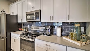 A modern kitchen with white cabinets, stainless steel appliances, a coffee maker, and a tray with bottles.