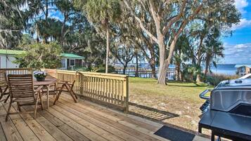 Une terrasse en bois avec une table et des chaises, un barbecue et une vue sur l’eau.