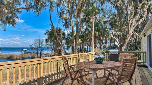 A wooden deck with a table and chairs, overlooking a body of water and trees. - 2 Living Rooms: Crescent City Home (Crescent City)