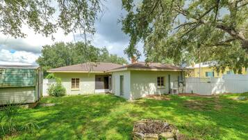 A single-story house with a front porch, a small yard with grass and a fire pit, and a tree with hanging branches.