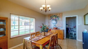 A dining area with a wooden table, chairs, a chandelier, and a window with blinds. - Lakefront Retreat on Lake Ariana w/ EV Charger (Auburndale)