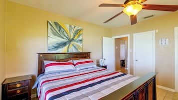 A bedroom with a bed, a ceiling fan, a painting, and a door.