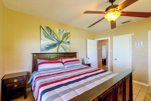 Un dormitorio con una cama, ventilador de techo, un cuadro y una puerta.