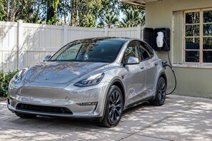 A silver Tesla Model 3 parked in a driveway with a white fence and trees in the background. - Lakefront Retreat on Lake Ariana w/ EV Charger (Auburndale)