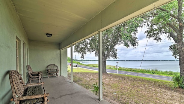 A covered porch with rustic wooden chairs and a view of a road and water body. - Lakefront Retreat on Lake Ariana w/ EV Charger (Auburndale)