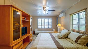A bedroom with a bed, a TV, a wardrobe, a ceiling fan, and a window with blinds.