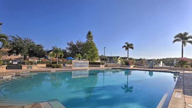 A clear swimming pool with a tiled deck, surrounded by palm trees and a clear blue sky.
