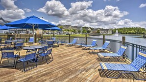 A wooden deck with blue chairs and tables, a fountain, and a lake view.
