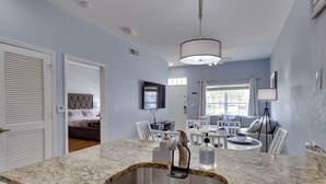 A modern kitchen with granite countertops, a stainless steel sink, and a dining area with white chairs and a table.