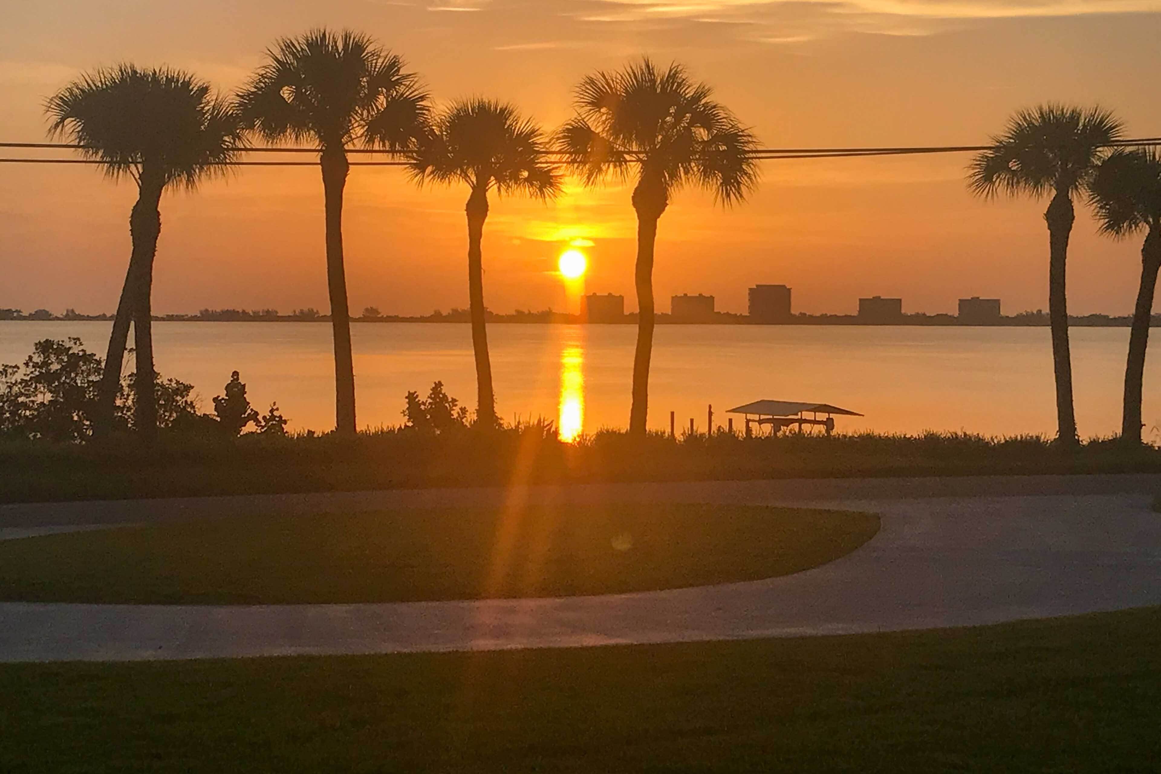 A sunset over a body of water with palm trees and a gazebo.