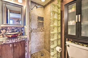Bathroom features a large mirror, sink with a unique basin, toilet, and shower with a glass enclosure.