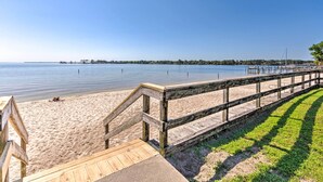 A wooden boardwalk leading to a sandy beach with a clear view of the water and distant shoreline. - Walk to Beach: Fort Walton Coastal Retreat (Fort Walton Beach)