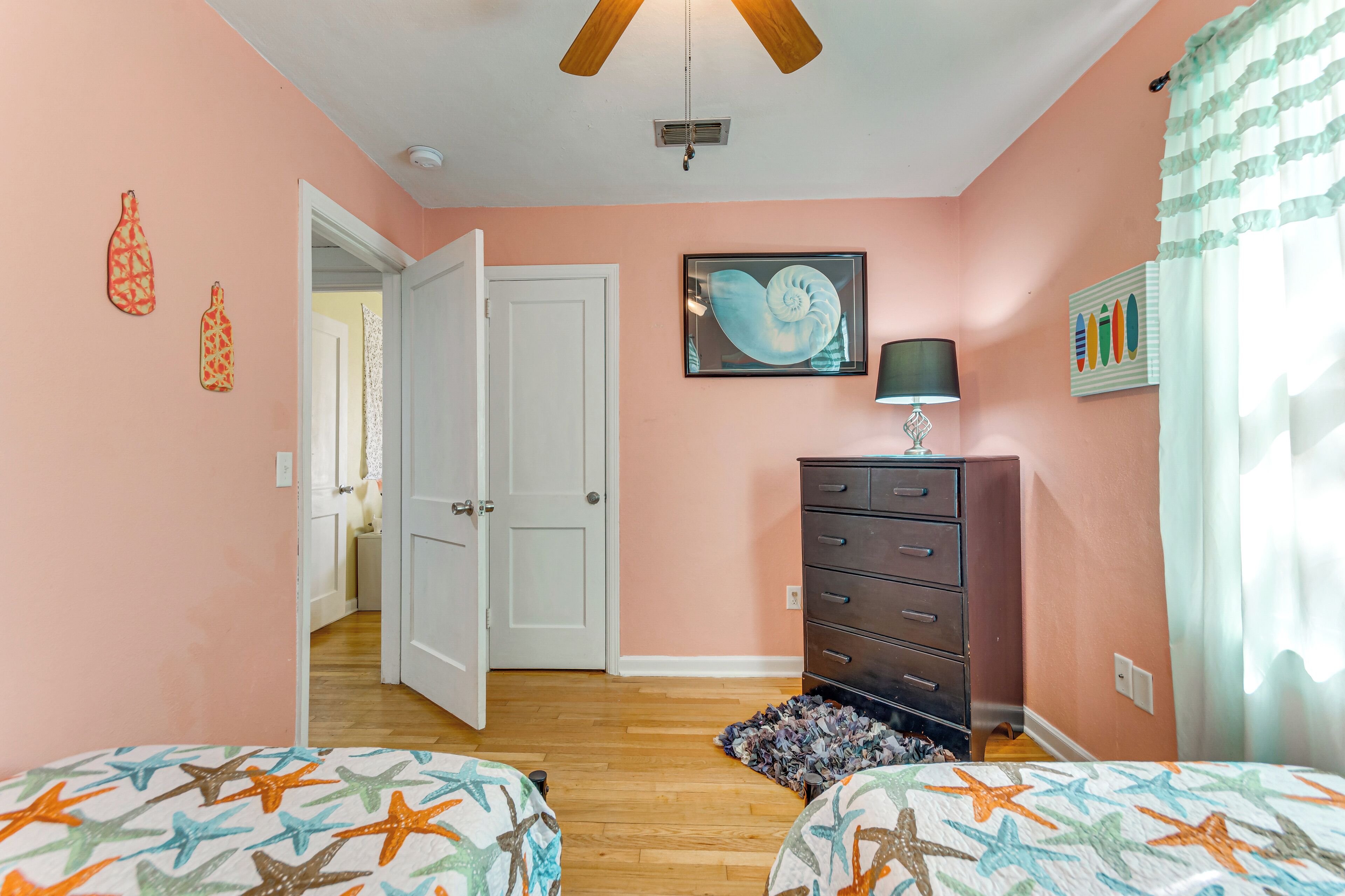 A bedroom with two beds, a dresser, a ceiling fan, and a door leading to another room.