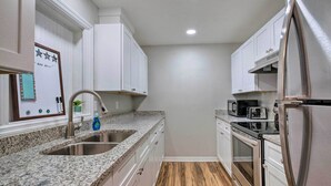 A kitchen with white cabinets, a granite countertop, stainless steel appliances, and a wooden floor.