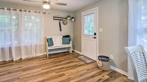 A room with a wooden floor, a white bench with blue cushions, a ceiling fan, a door with a window, and a basket labeled "Shoes".