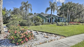 A residential house with a well-maintained lawn, palm trees, and a garden with red flowers. - Luxurious Home w/ Private Pool & Lanai Near Tampa! (Odessa)