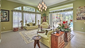 A spacious living room with a large chandelier, comfortable seating, and a view through a glass door. - Luxurious Home w/ Private Pool & Lanai Near Tampa! (Odessa)