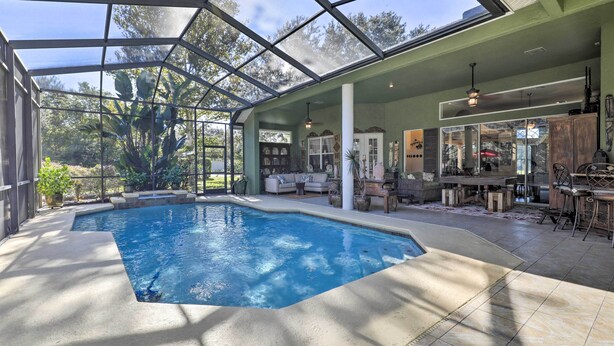 A covered swimming pool with a glass ceiling, surrounded by indoor seating and a patio area. - Luxurious Home w/ Private Pool & Lanai Near Tampa! (Odessa)