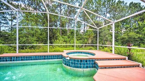 Une piscine avec un jacuzzi, entourée d’une structure métallique blanche et d’une végétation luxuriante.