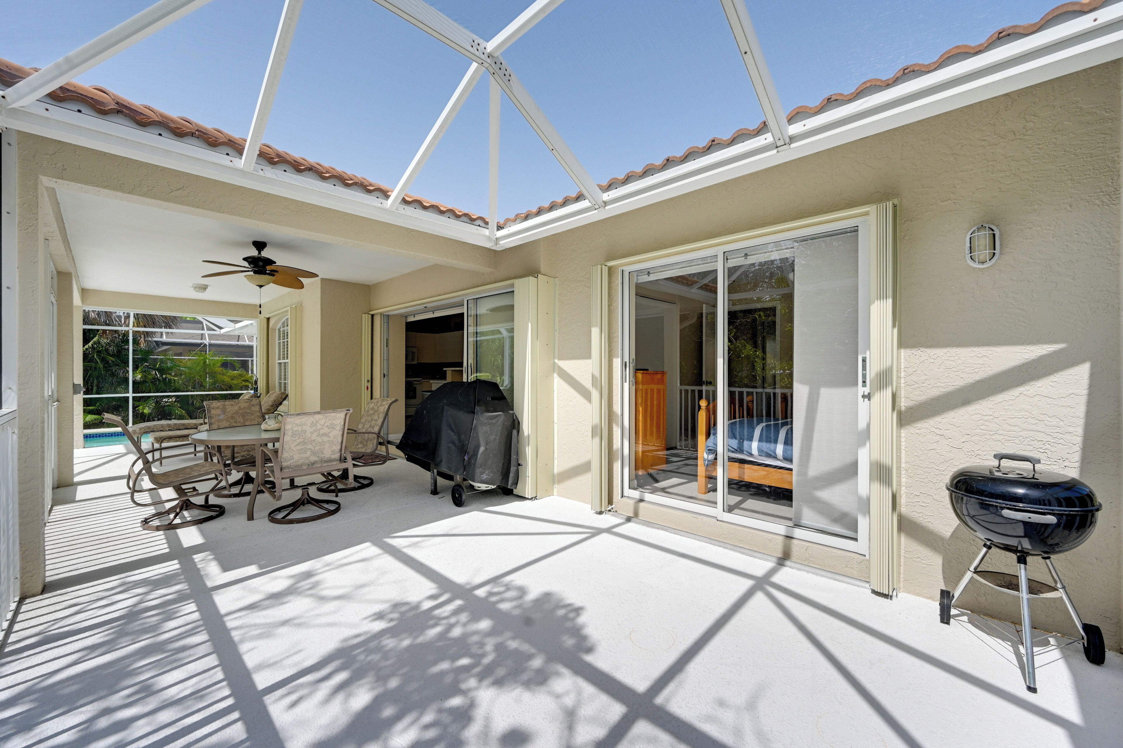Une terrasse couverte avec une table et des chaises, un ventilateur de plafond, un barbecue et une porte-fenêtre coulissante donnant sur un balcon.