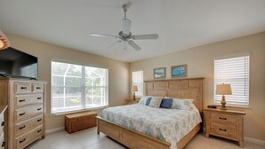 A bedroom with a bed, wooden nightstands, a dresser, a ceiling fan, and large windows. - Sunny Marco Island House < 3 Blocks to Beach! (Marco Island)