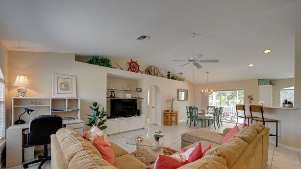 A spacious living room with a large beige sofa, a glass coffee table, and a TV. There is a dining area with a table and chairs, and a ceiling fan. - Sunny Marco Island House < 3 Blocks to Beach! (Marco Island)